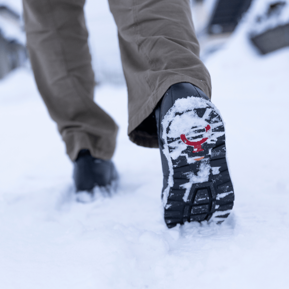 Person wearing black winter apres snow boots with a snow-covered sole in the snow.