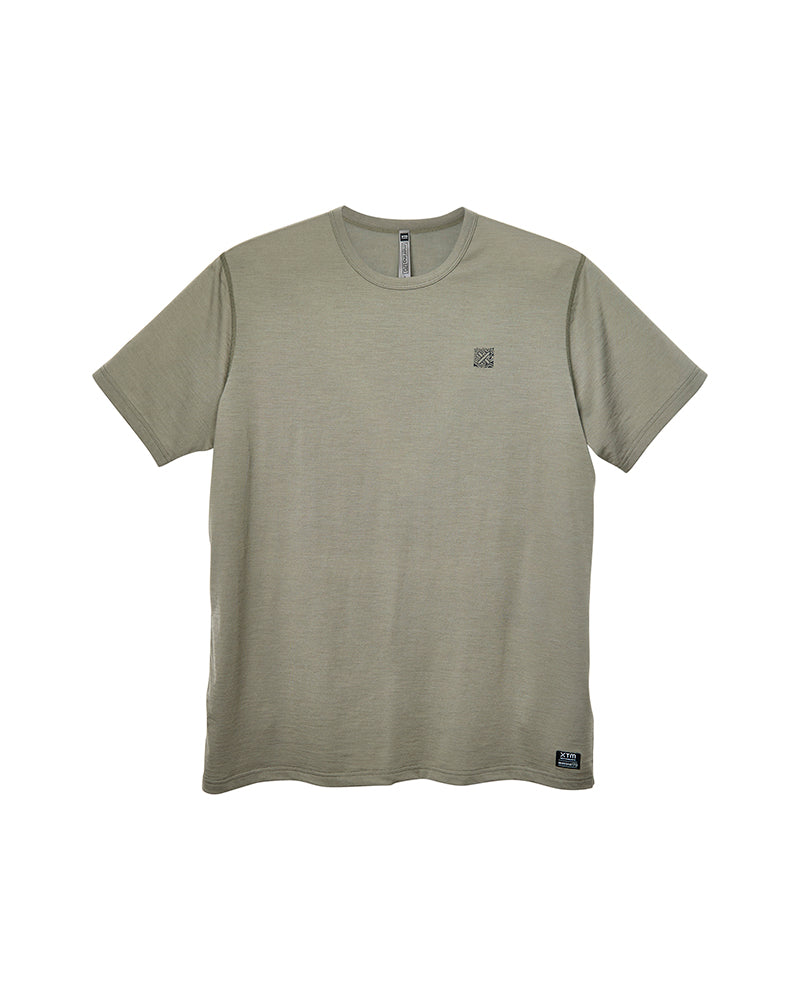 A short-sleeve crewneck t-shirt in a muted sage green color, featuring a small dark square logo on the left chest and a small brand tag near the bottom hem, displayed against a plain white background. XTM khaki merino thermal mens