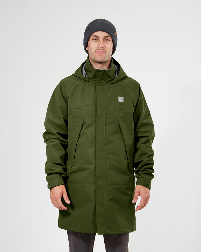 A man wearing a dark olive green hooded jacket and a dark gray beanie, standing against a light gray studio background. khaki XTM unisex