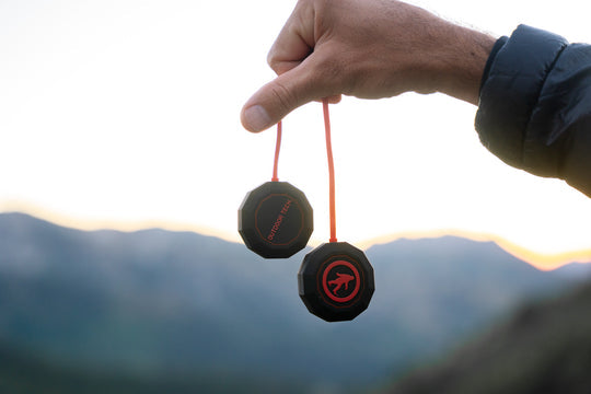 Hand holding a black and red object against a mountainous background