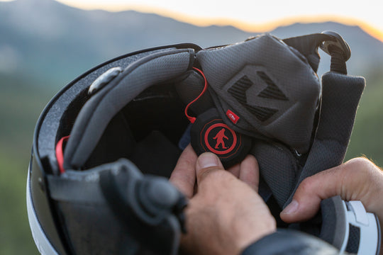 Person adjusting a black helmet with a red logo against a blurred natural background